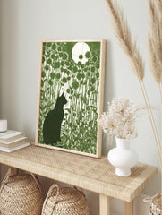Green linocut print of a black cat silhouette in a field of flowers under a large white moon, in an alternate framed mockup