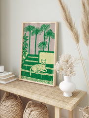 Green cat wall art illustration with a cat lying on steps, surrounded by palm trees and plants on a light purple background. - Image 3
