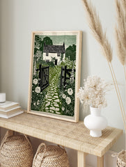 Green linocut print of a British cottage garden with open gate, cobbled path, foxgloves, and, in an alternate framed mockup