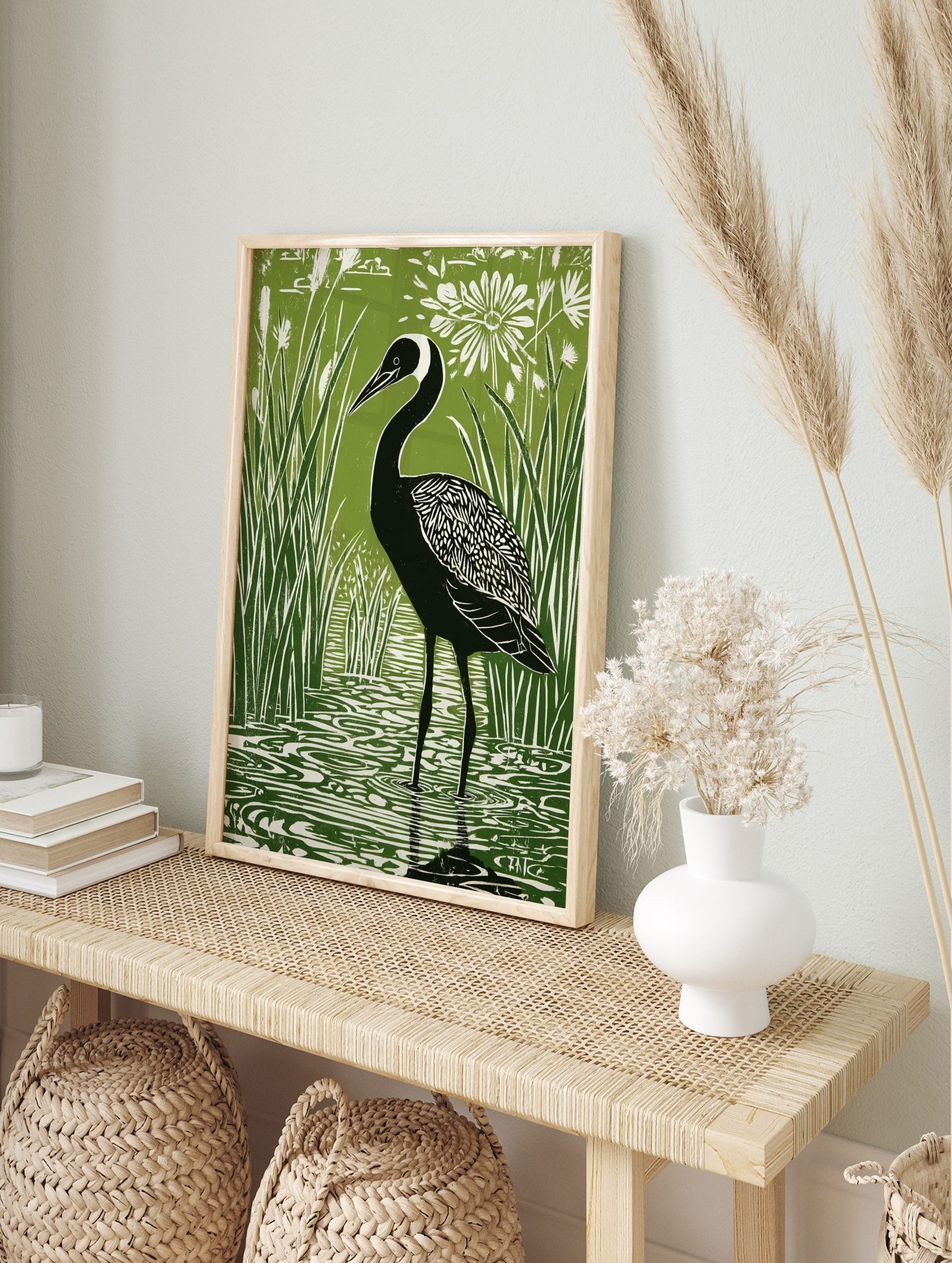 Green and white linocut style print of a black crane bird in reeds and water with a white, in an alternate framed mockup