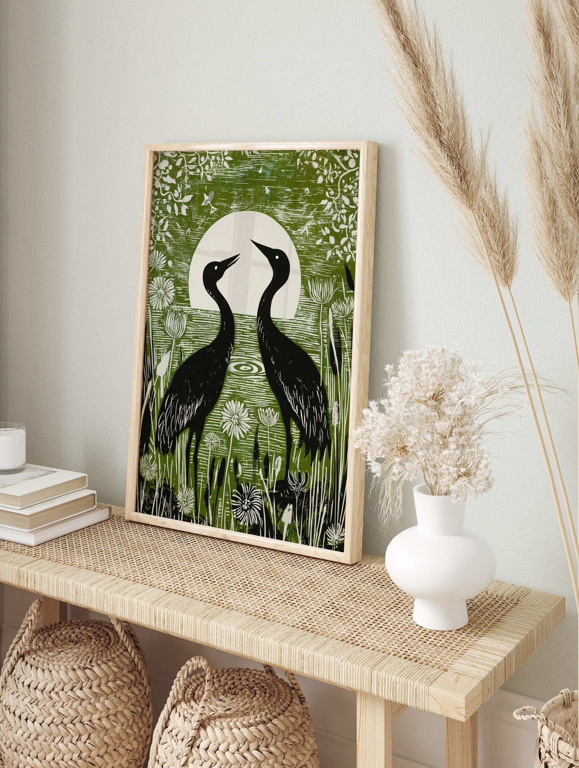Green linocut style print of two black crane birds facing a white full moon in a wetland with, in an alternate framed mockup
