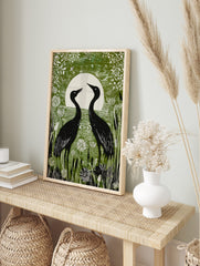 Green linocut style print of two black crane birds facing a white full moon in a wetland with, in an alternate framed mockup