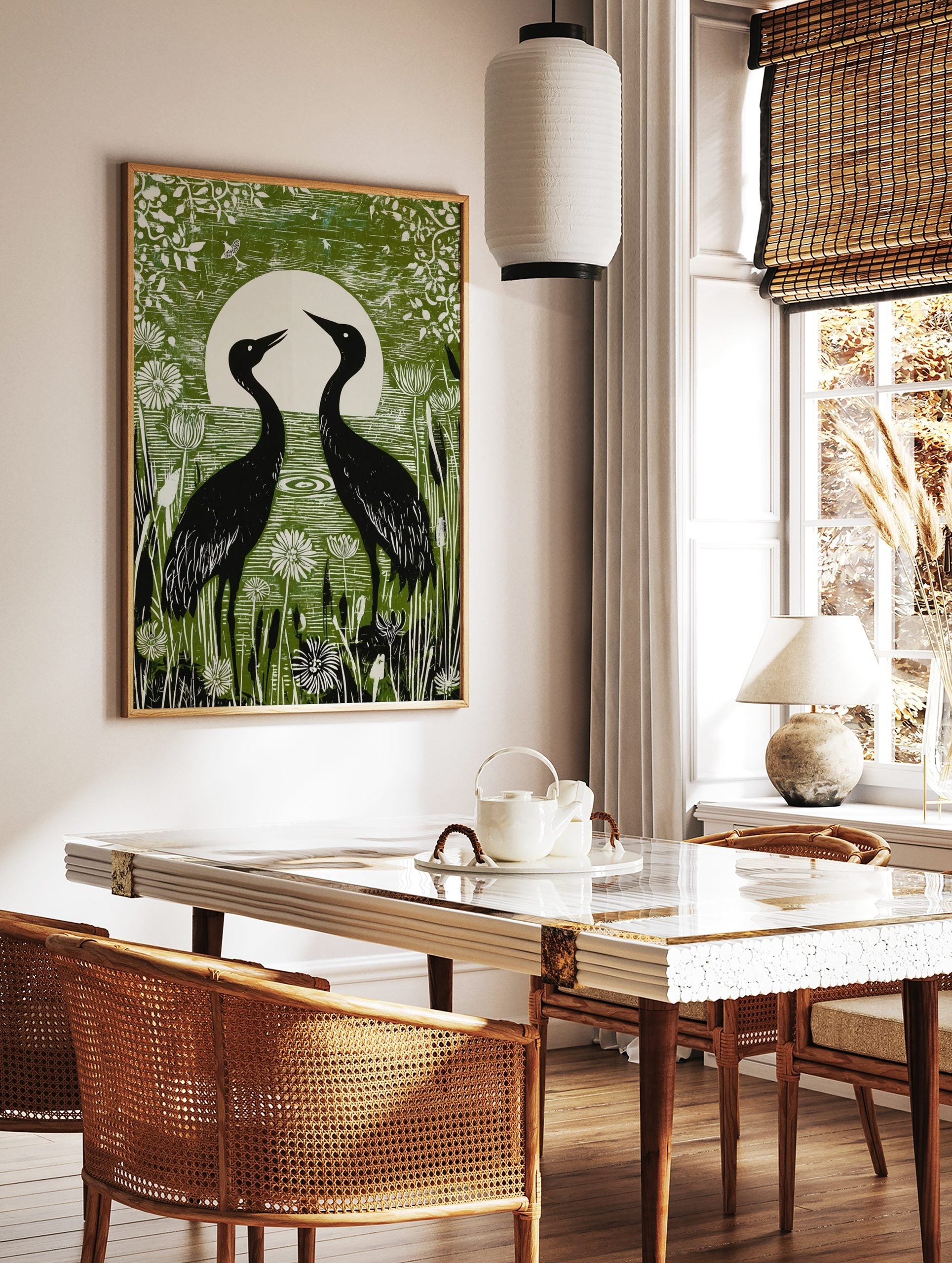 Green linocut style print of two black crane birds facing a white full moon in a wetland with white, in a styled room mockup