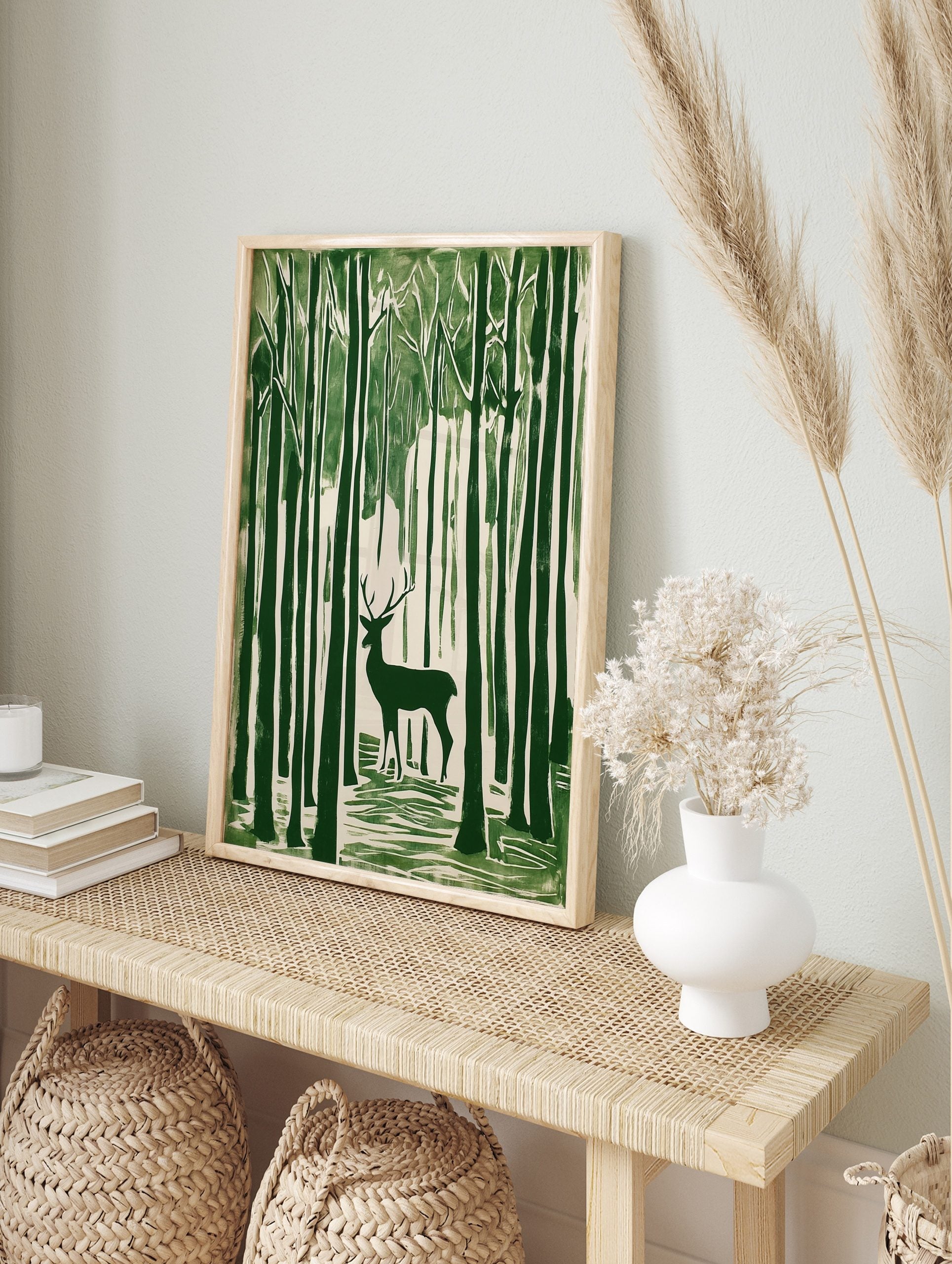 Green linocut style art print of a stag with antlers standing amongst tall forest trees, in an alternate framed mockup