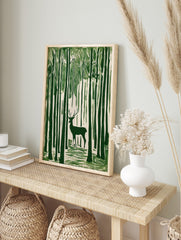 Green linocut style art print of a stag with antlers standing amongst tall forest trees, in an alternate framed mockup