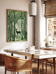 Green linocut style art print of a stag with antlers standing amongst tall forest trees, in a styled room mockup