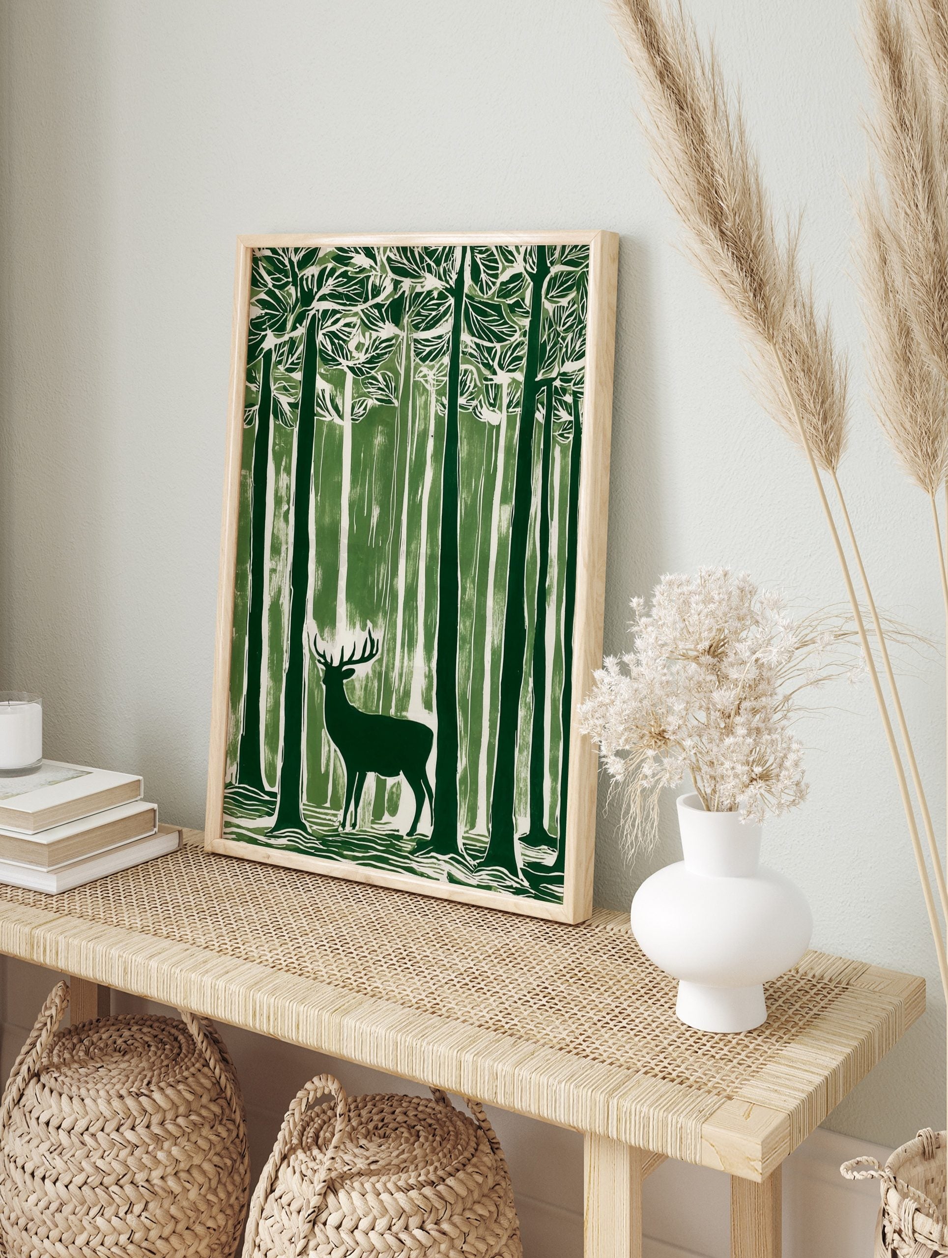 Green linocut style art print of a stag with antlers standing in a dense forest of tall trees, in an alternate framed mockup