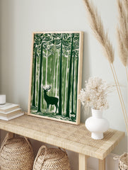 Green linocut style art print of a stag with antlers standing in a dense forest of tall trees, in an alternate framed mockup