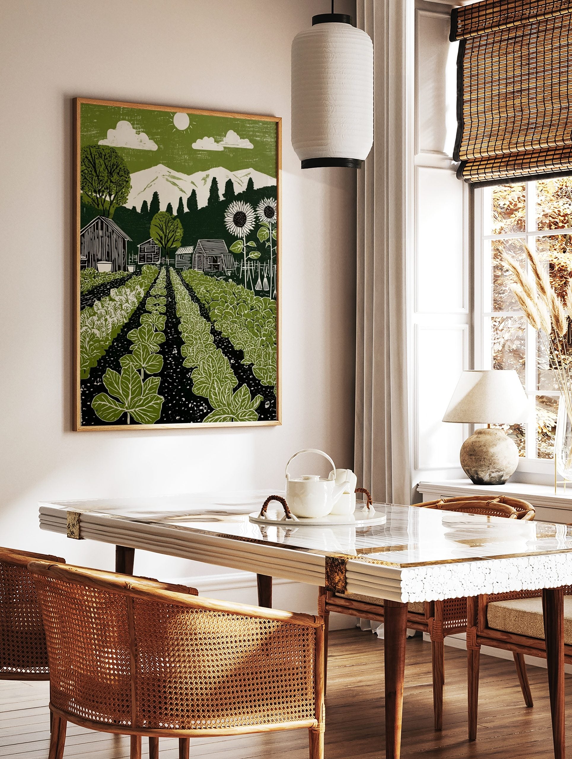 Green garden linocut-style print with vegetable rows, barns, sunflowers, mountains, and sun in sky, in a styled room mockup
