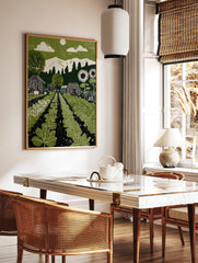 Green garden linocut-style print with vegetable rows, barns, sunflowers, mountains, and sun in sky, in a styled room mockup