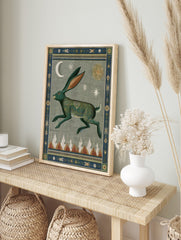 Stylized green hare wall art print with intricate patterns, crescent moon, sun, stars, and mountain peaks, bordered by decorative motifs, displayed as the same artwork in an alternate framed wall art mockup