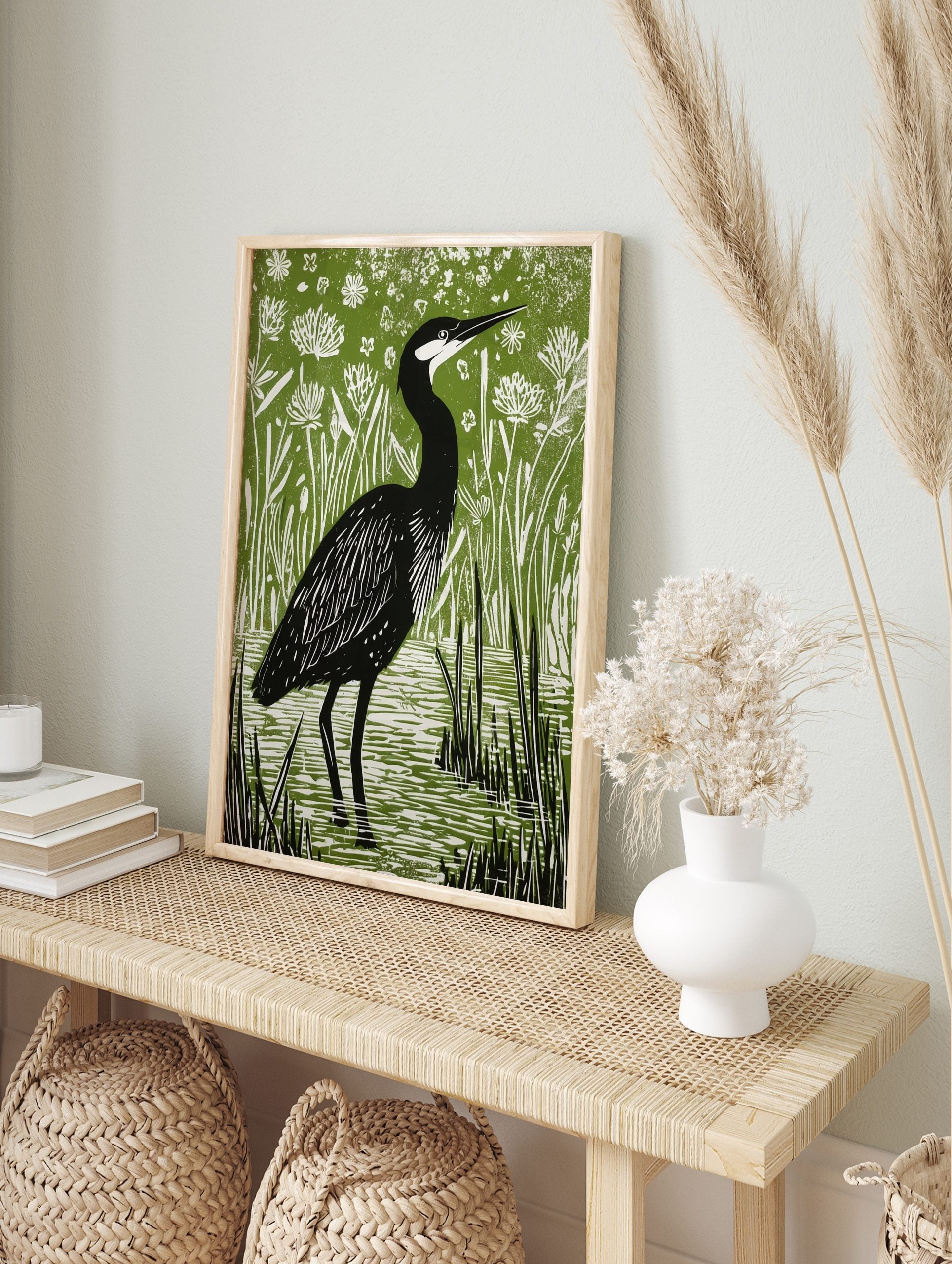 Illustrative linocut print of a black heron with white head markings, standing in green marsh, in an alternate framed mockup