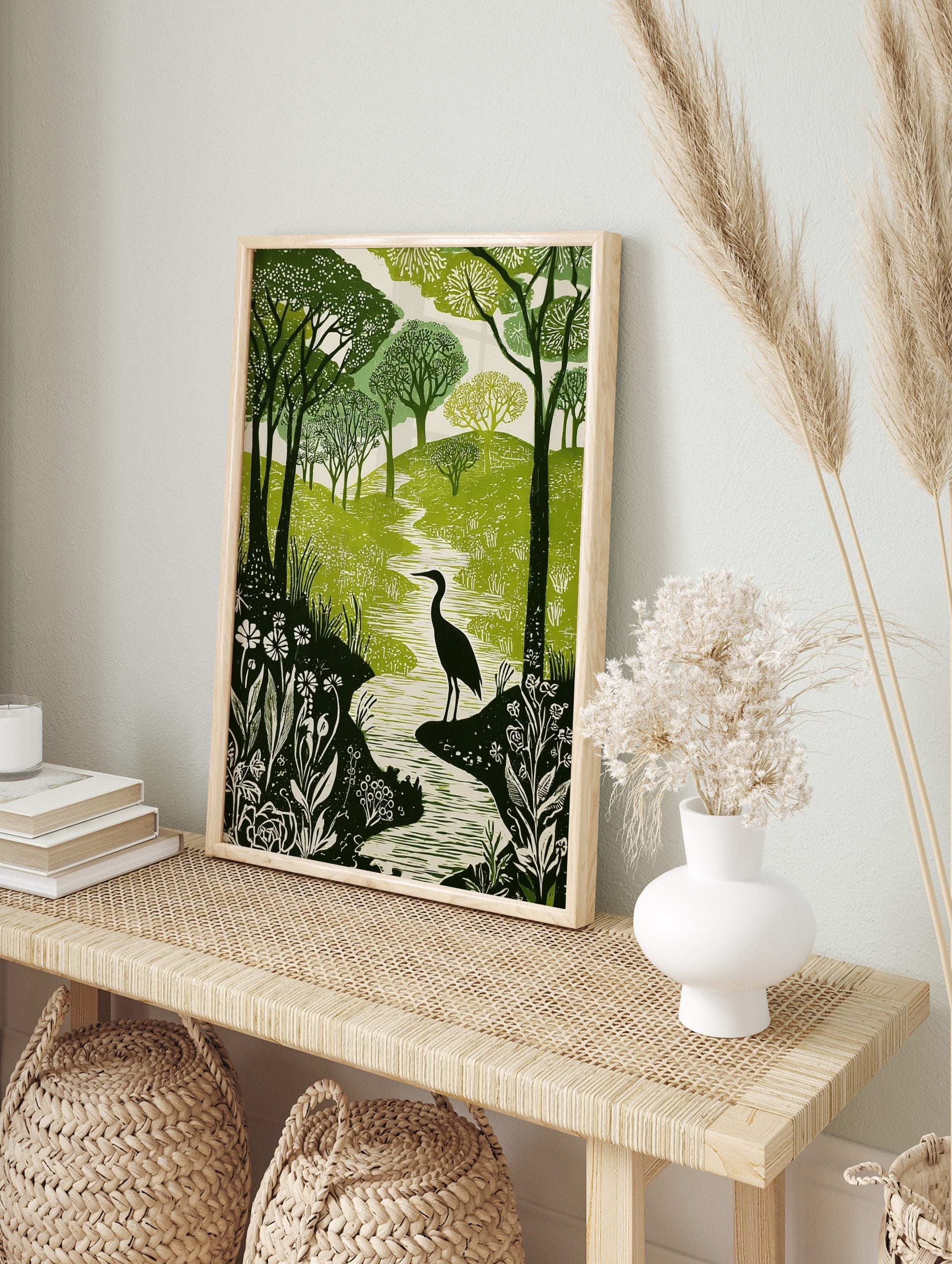 Green and white woodcut print of a heron in a winding river, surrounded by forest trees and, in an alternate framed mockup