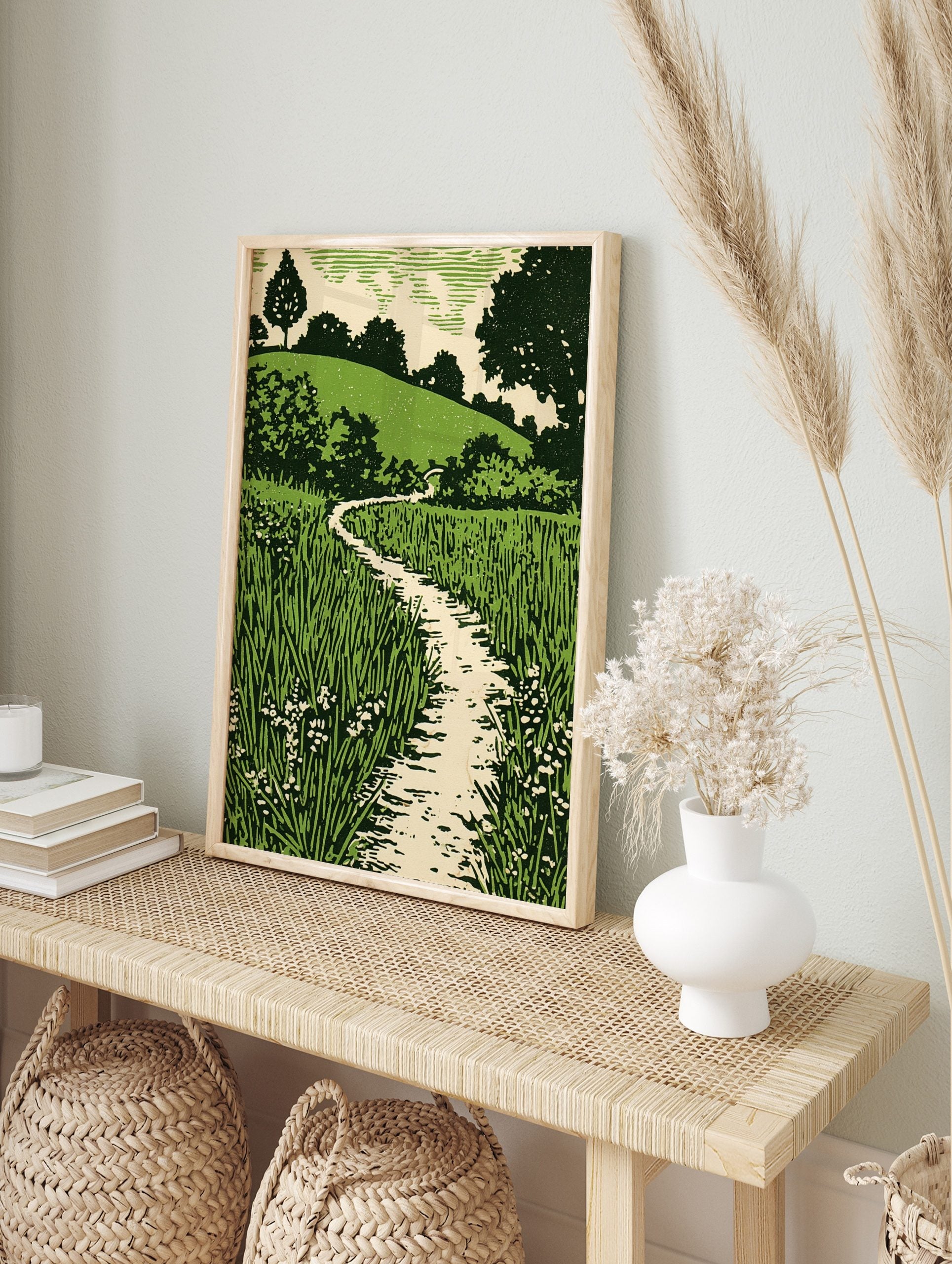Green landscape woodcut style print with winding path, tall grass, small flowers, and, in an alternate framed mockup