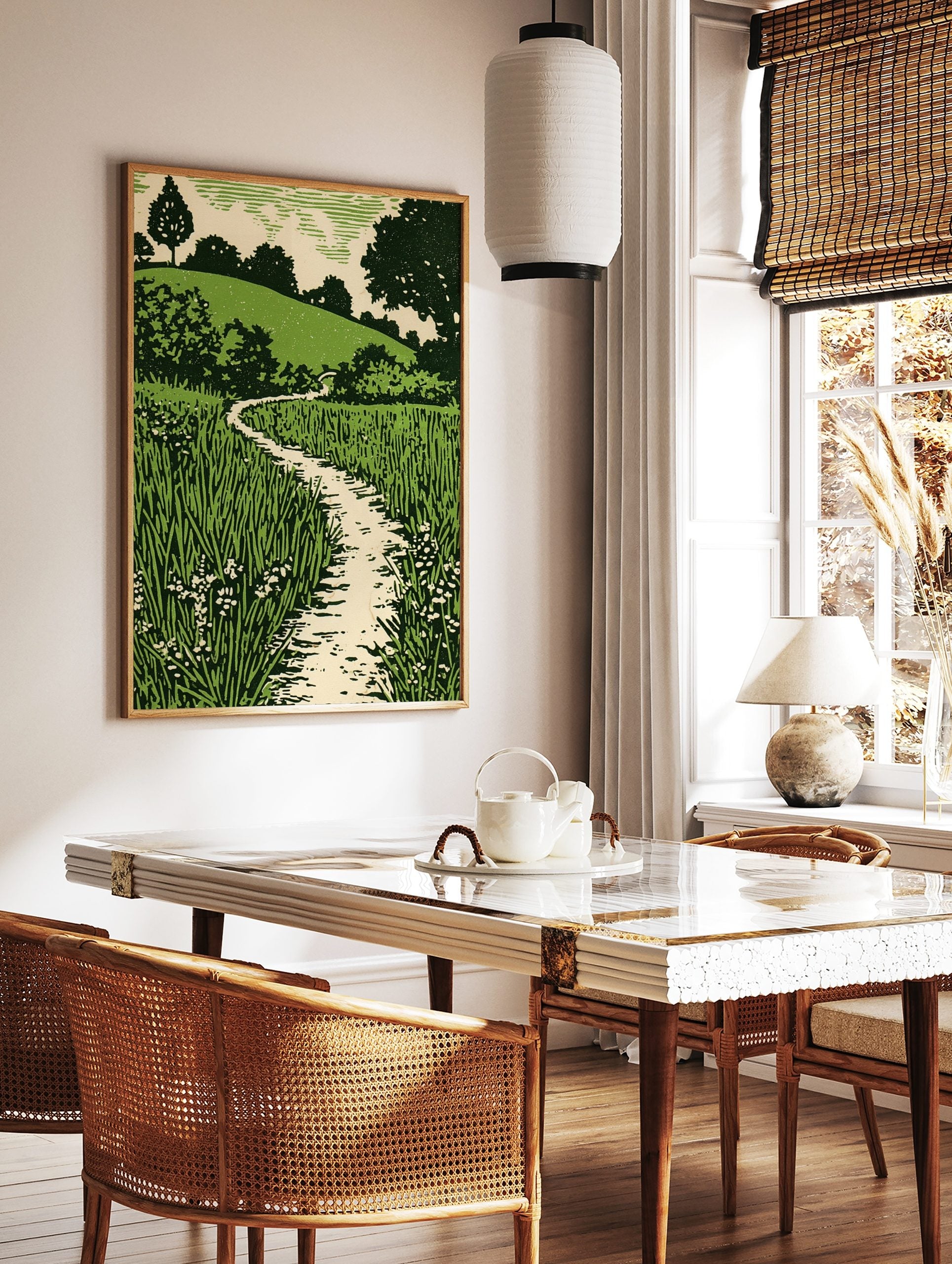 Green landscape woodcut style print with winding path, tall grass, small flowers, and tree-covered, in a styled room mockup