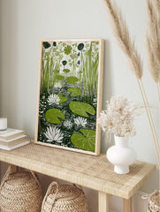 Green lily pads, white water lilies, and tall reeds in a pond, linocut-style botanical print, in an alternate framed mockup