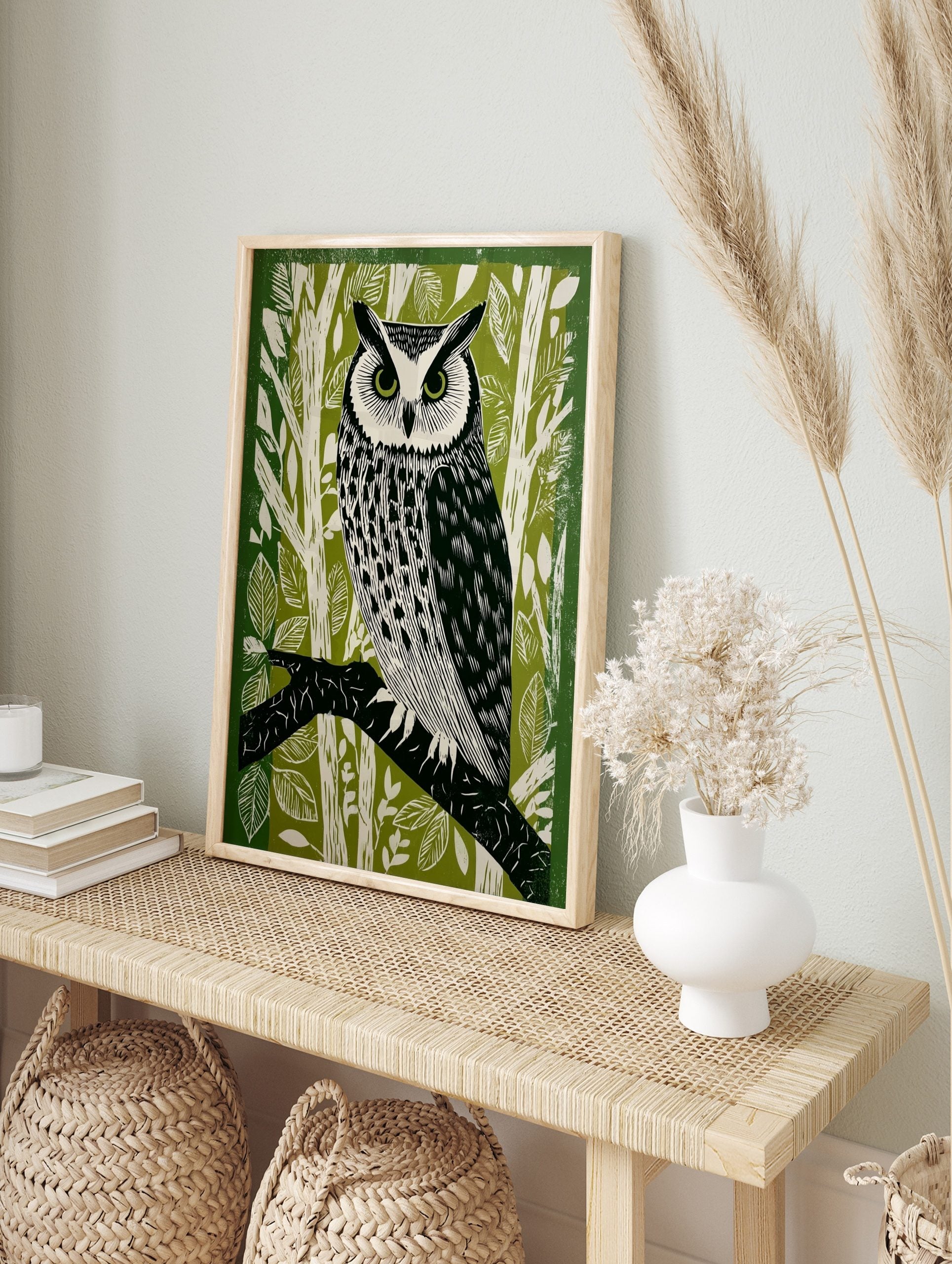 Illustrative lino print of a long-eared owl with green eyes, perched on a branch, set against, in an alternate framed mockup