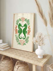 Green seahorses forming a heart, surrounded by orange coral and green seaweed, with scallop, in an alternate framed mockup