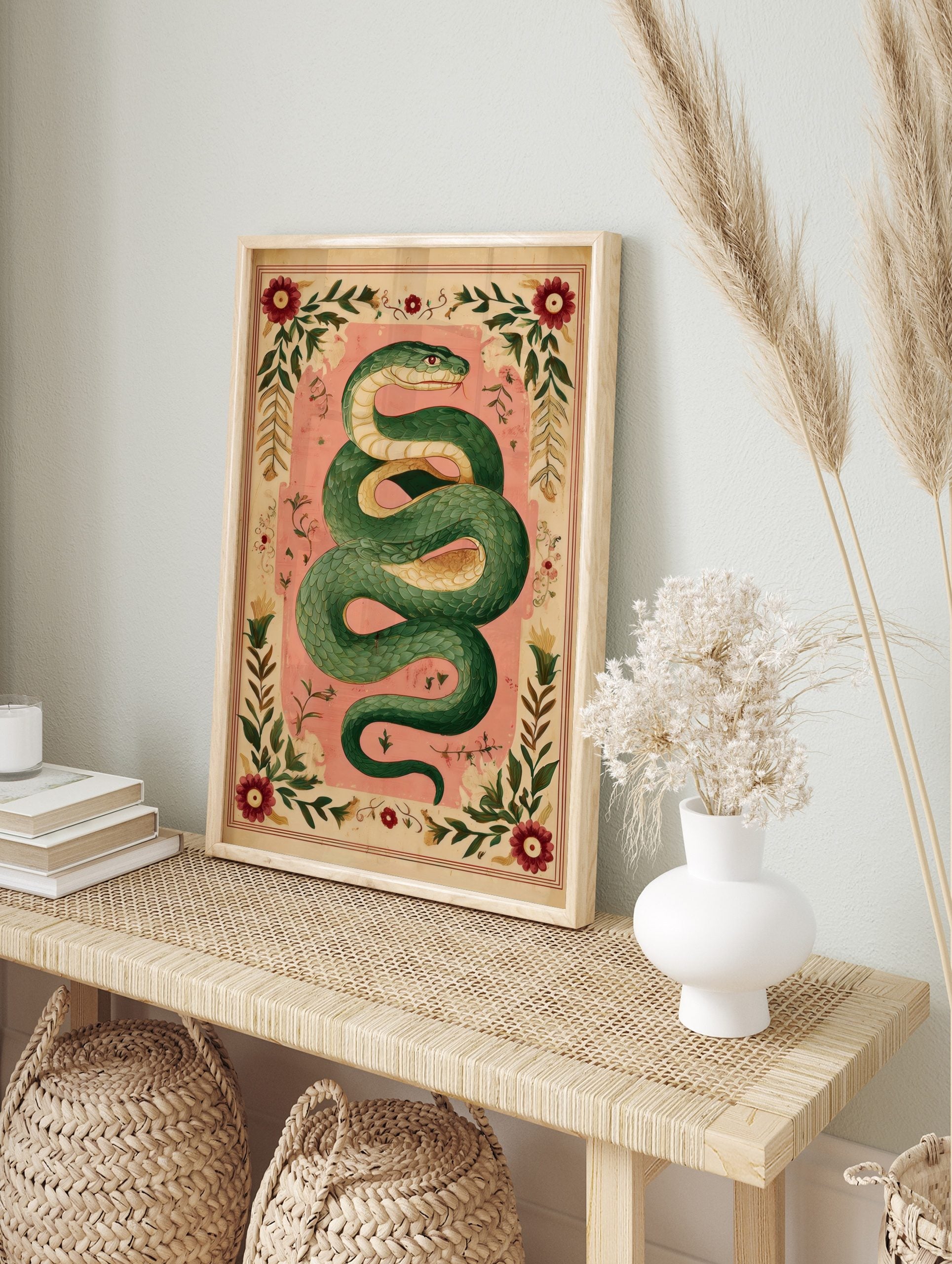 Illustrative green serpent coiled on a pink background, surrounded by an ornate border of red flowers and green leaves, in