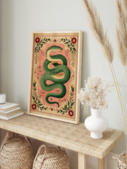 Illustrative green serpent coiled on a pink background, surrounded by an ornate border of red flowers and green leaves, in