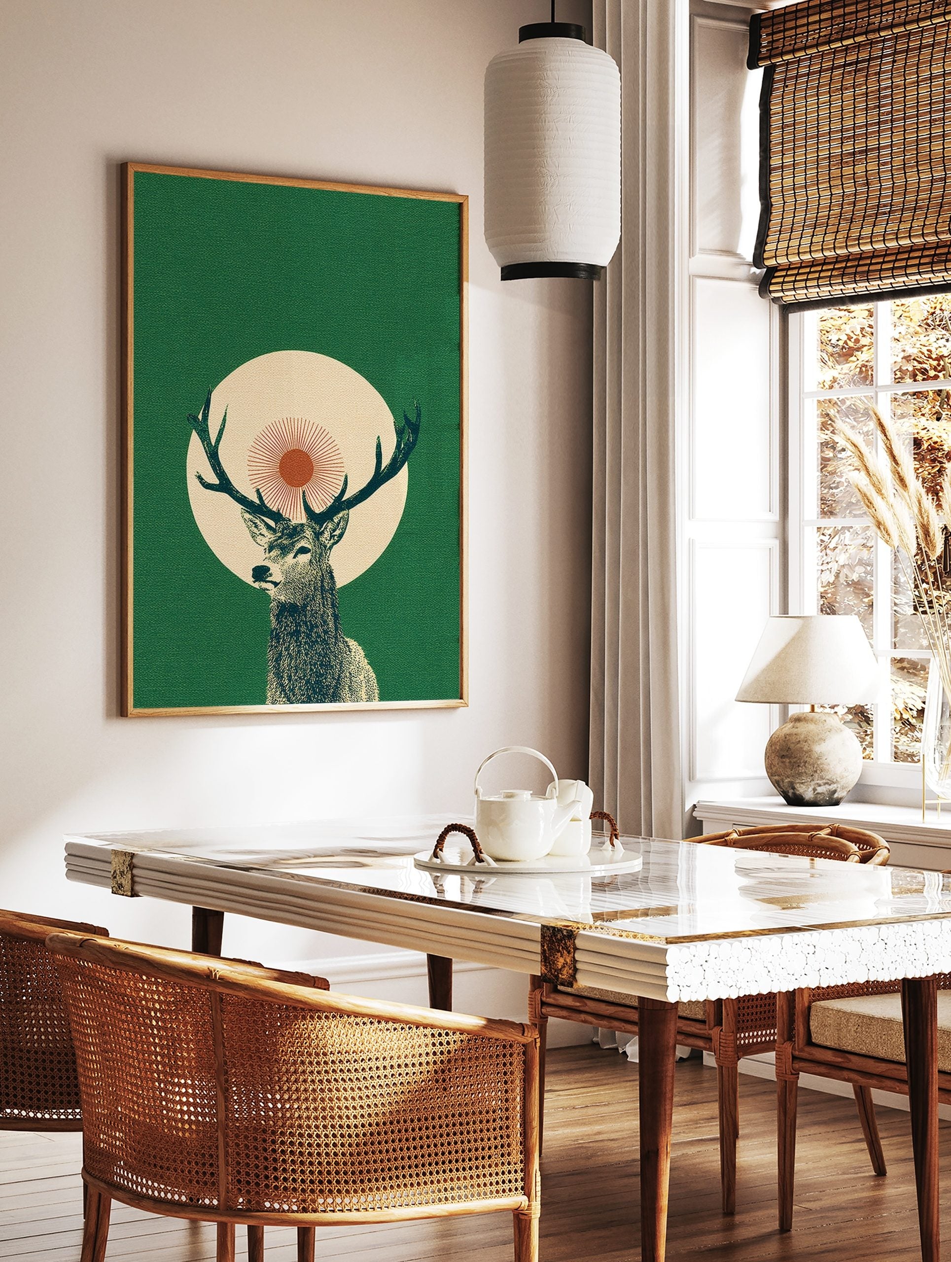 Illustrative green stag with antlers, set against a cream circle and red sunburst on a dark green, in a styled room mockup
