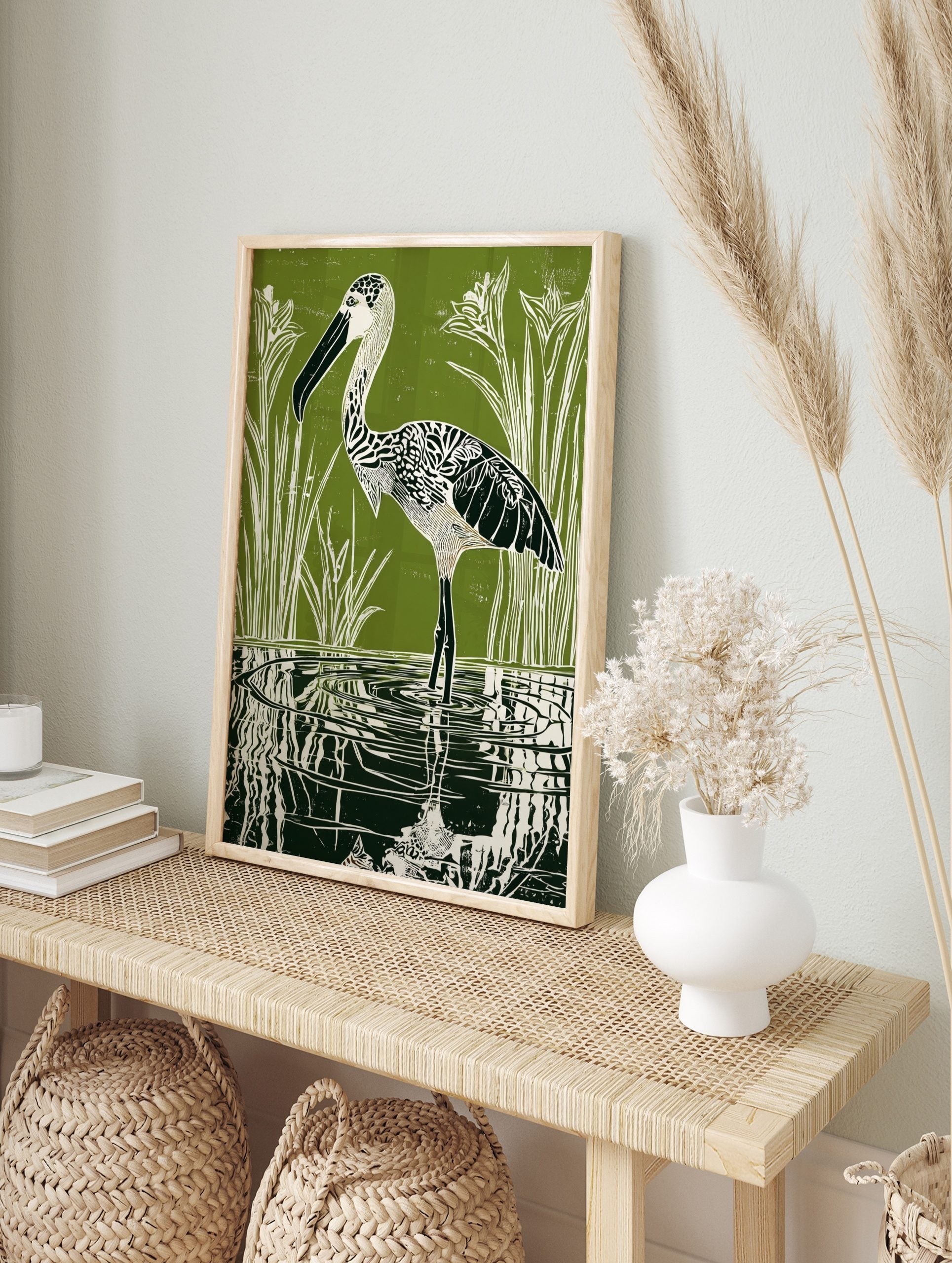 Green linocut print of a patterned stork wading in water with reeds and reflections, in an alternate framed mockup