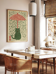 Illustrative green striped cat under a red umbrella with green raindrops on a cream background, in a styled room mockup