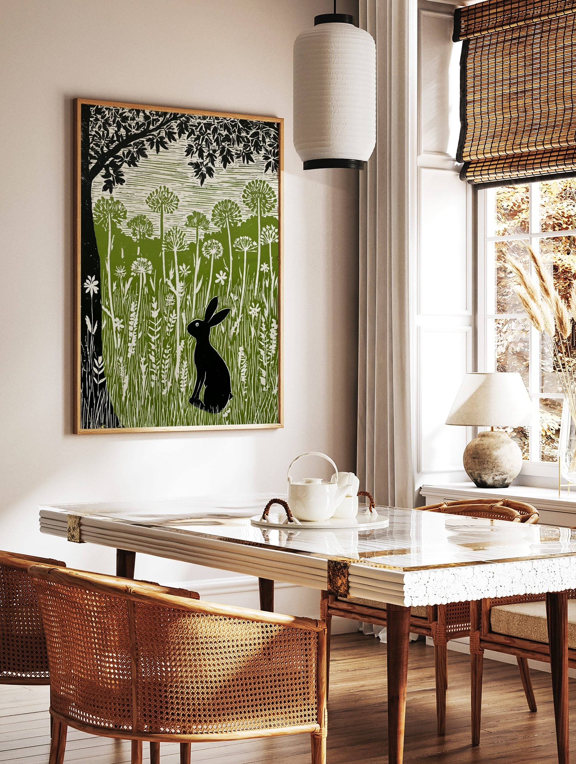 Linocut print of a black hare in a green meadow with tall white wildflowers and a large black tree, in a styled room mockup