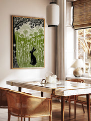 Linocut print of a black hare in a green meadow with tall white wildflowers and a large black tree, in a styled room mockup