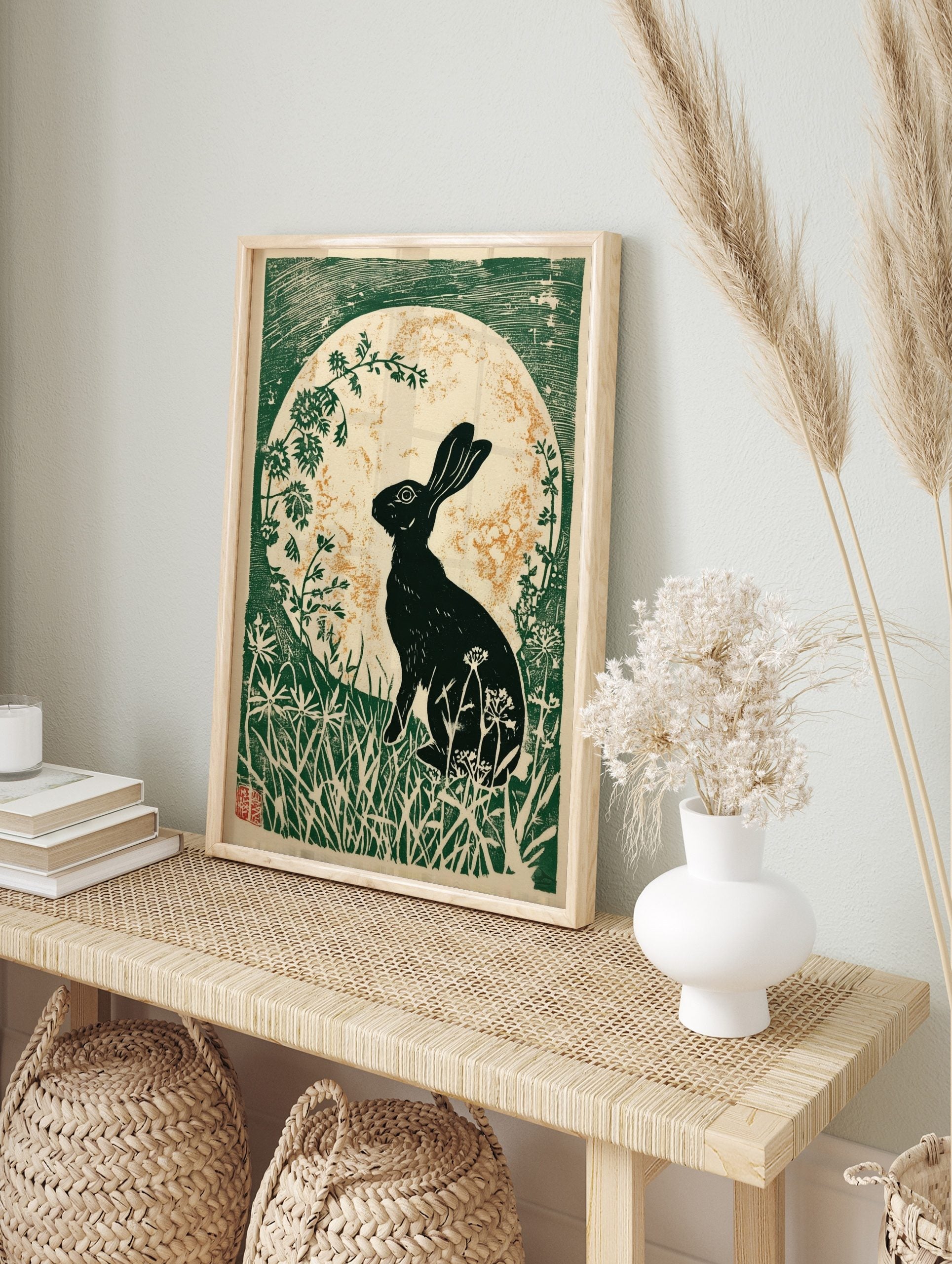 Black hare silhouette against a gold speckled moon, surrounded by green foliage in a linocut, in an alternate framed mockup