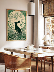 Green linocut print of a hare in silhouette looking at a large full moon, surrounded by grass and, in a styled room mockup