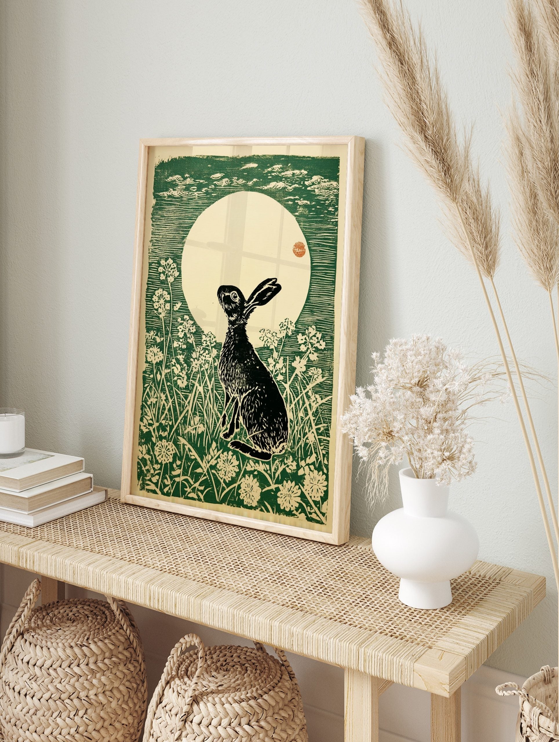 Woodcut print of a black hare looking up at a large cream moon with green sky and white, in an alternate framed mockup