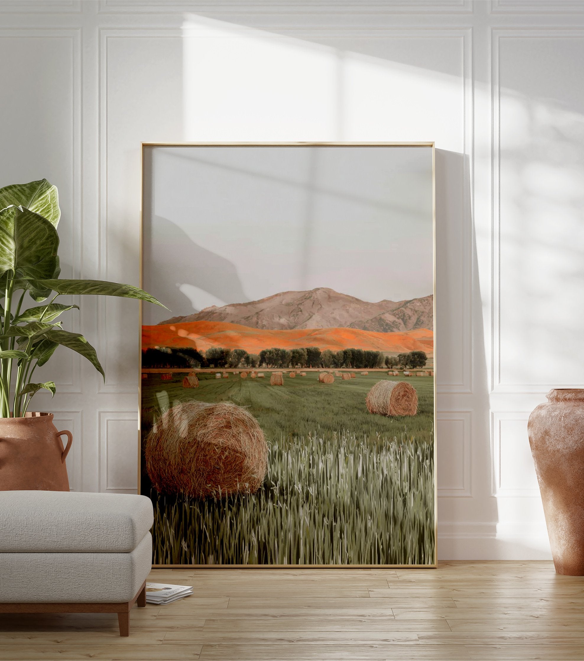 Photographic print of a field with hay bales, green grass, a row of trees, orange hills, and mountains under a grey sky. - Image 3