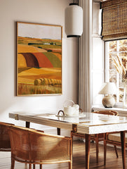 Illustrative landscape wall art of golden hay bales in a field with a distant farmstead and rolling, in a styled room mockup