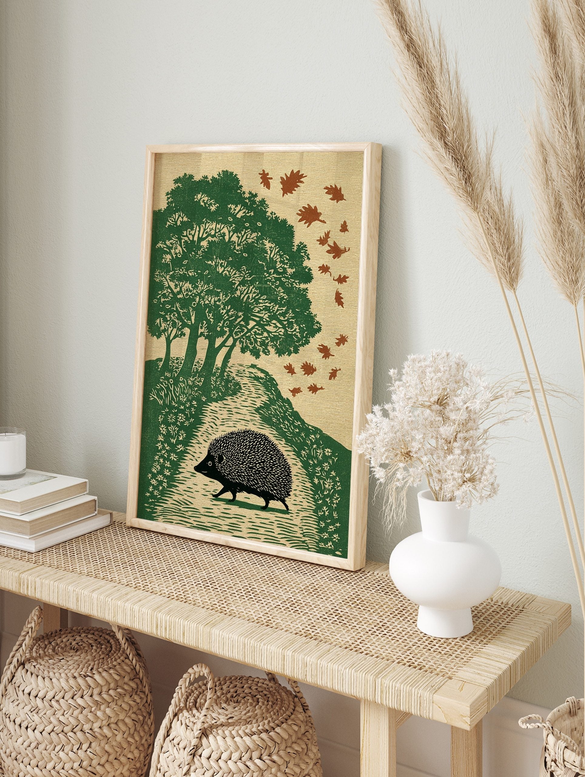Illustrative print of a black hedgehog walking on an autumn path with green trees and falling, in an alternate framed mockup