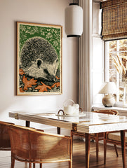 Linocut print of a hedgehog with black quills, off-white face, orange autumn leaves, and green, in a styled room mockup