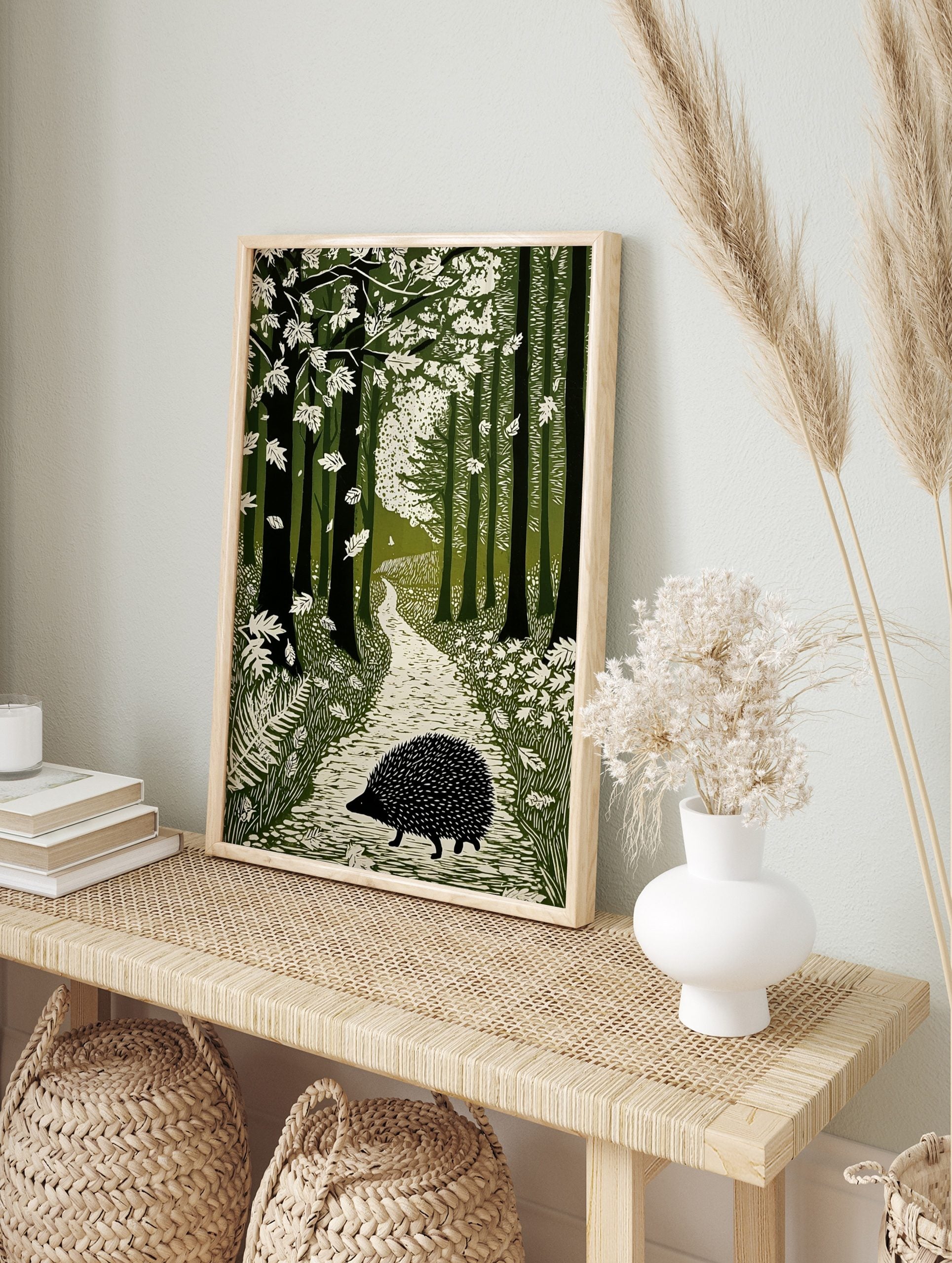 Linocut-style art print of a hedgehog on a winding path through a green forest with falling, in an alternate framed mockup
