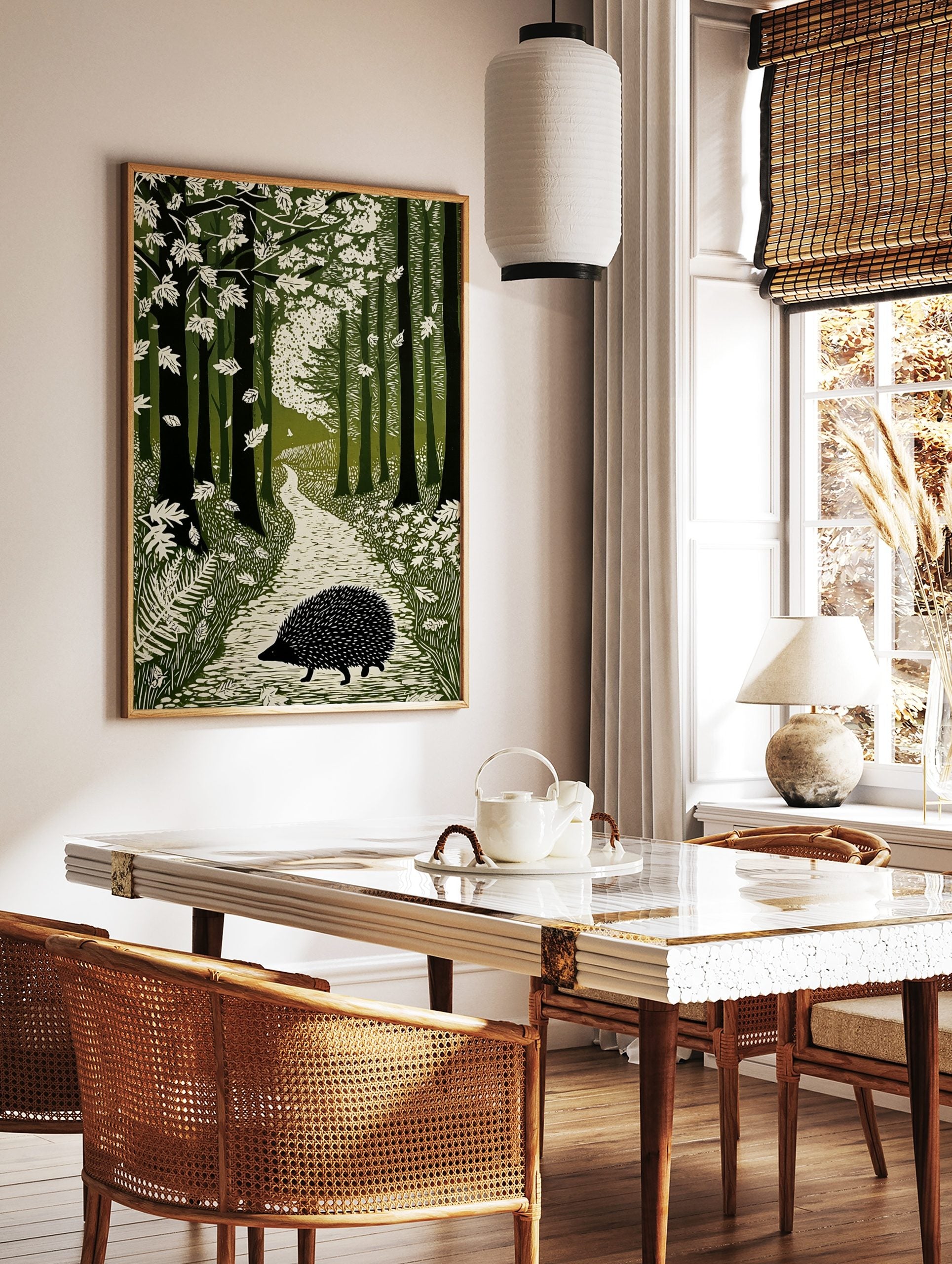 Linocut-style art print of a hedgehog on a winding path through a green forest with falling leaves, in a styled room mockup