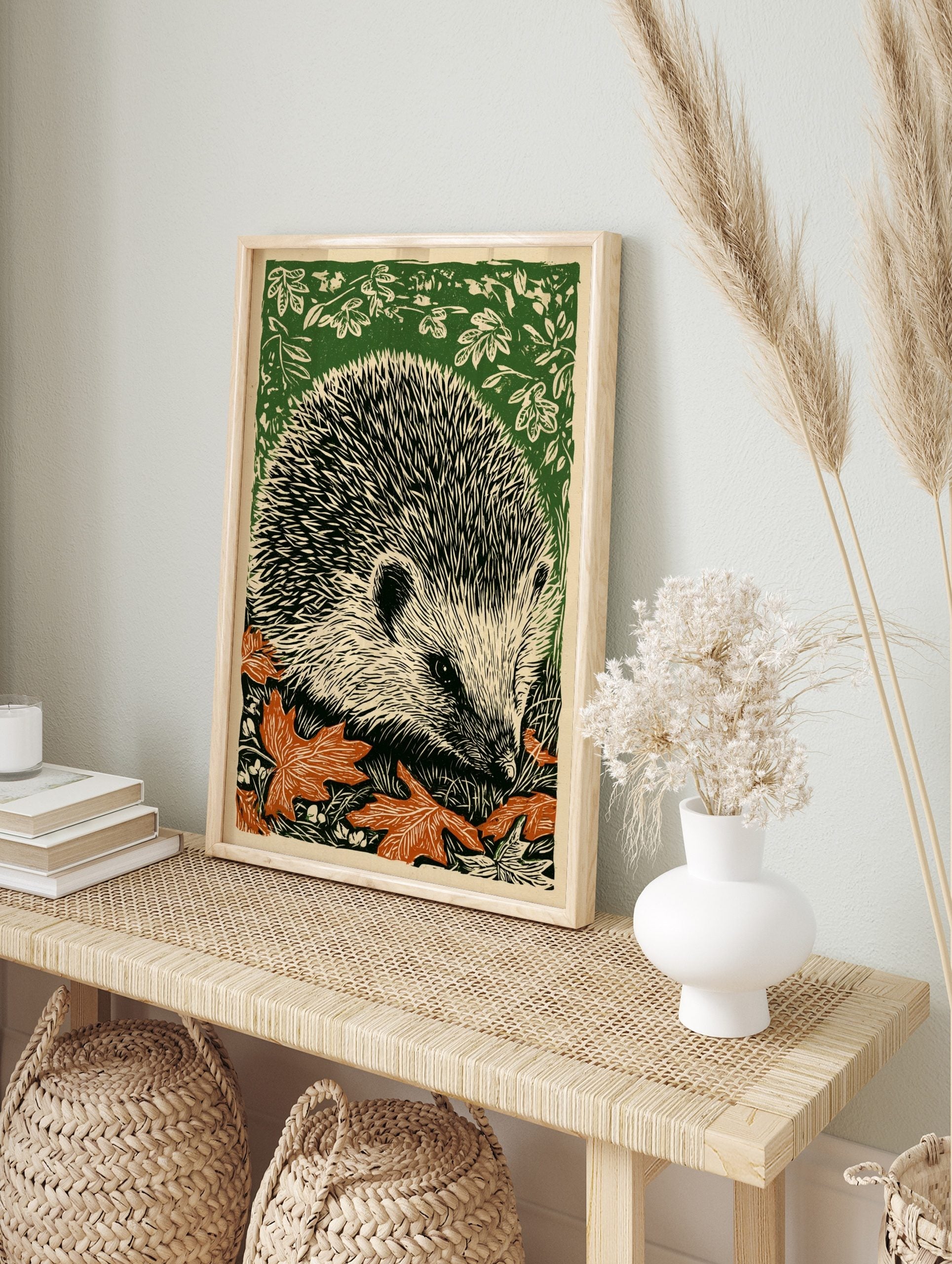 Woodcut style art print of a hedgehog amongst green foliage and orange autumn leaves, facing, in an alternate framed mockup