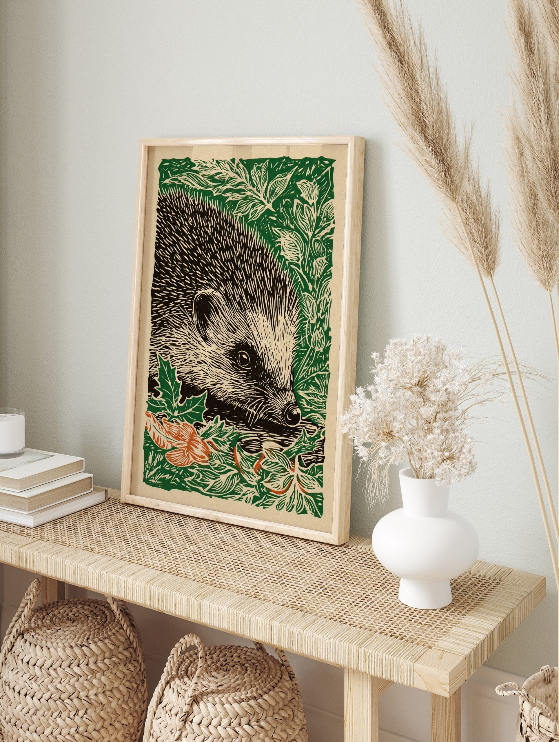 Woodcut illustration art print of a hedgehog in green foliage with some orange autumn leaves, in an alternate framed mockup