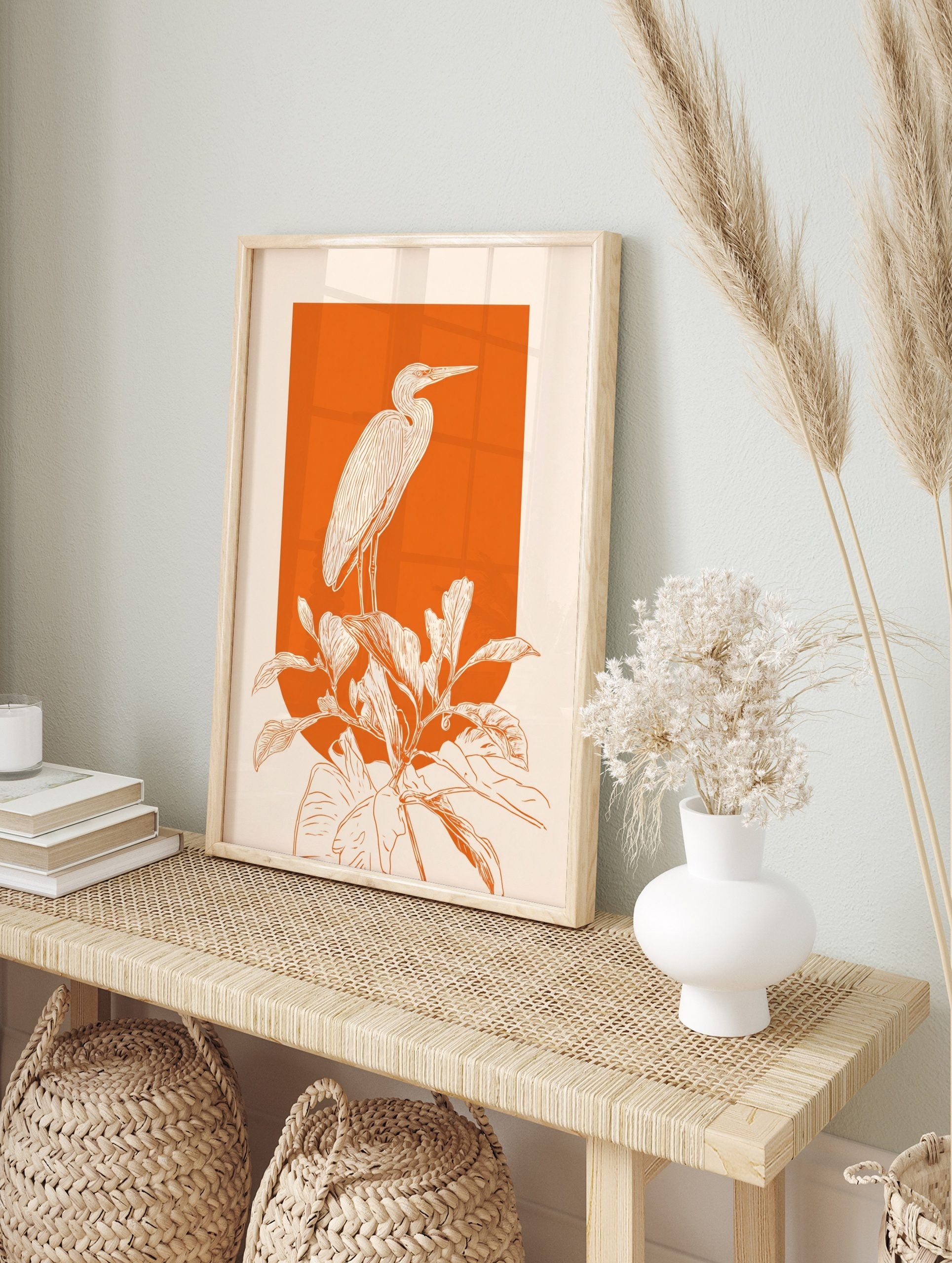 White line art illustration of a heron standing on large plants against a vibrant orange, in an alternate framed mockup