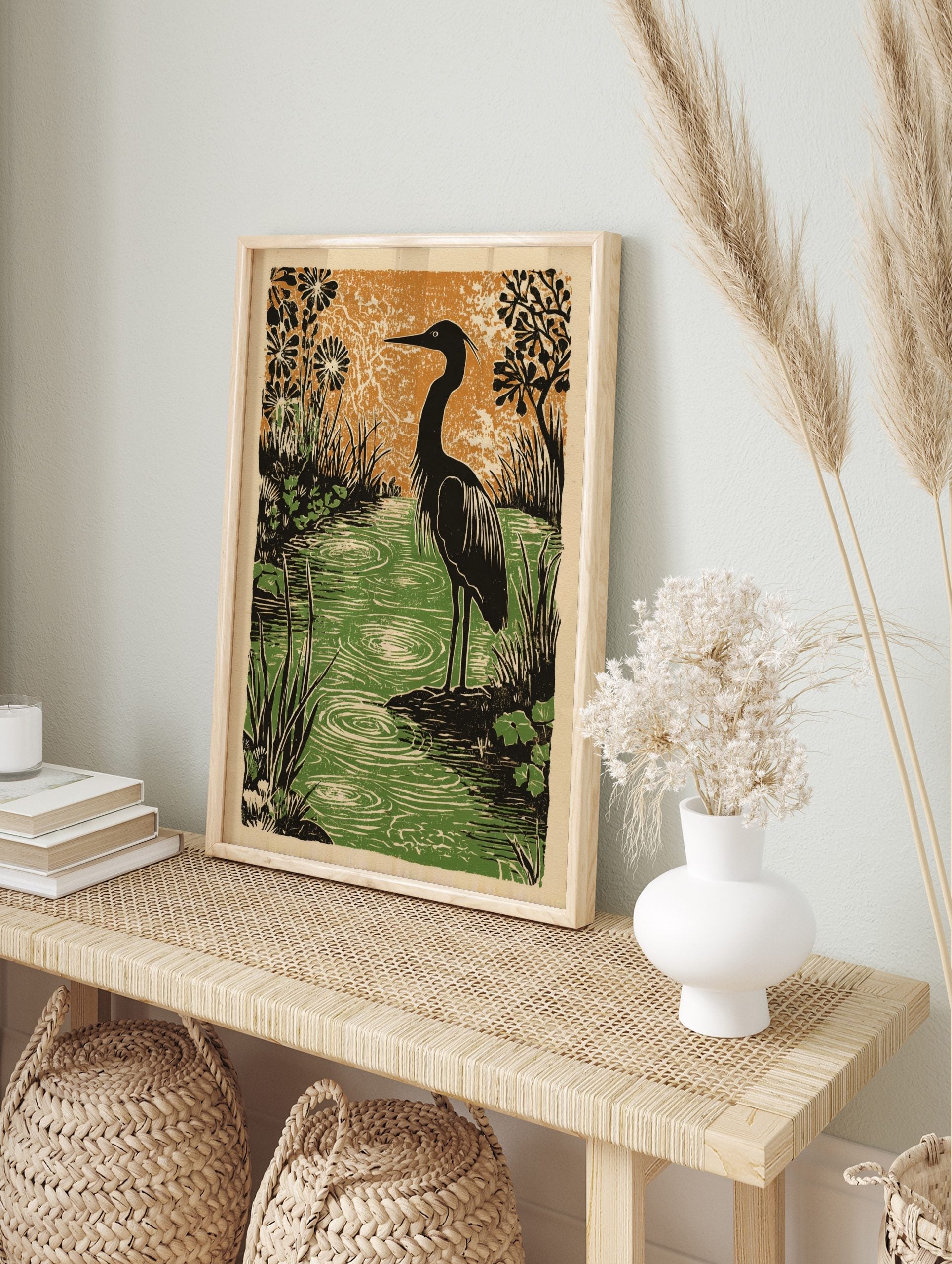 Illustrative woodcut print of a dark heron in a green pond with ripples, surrounded by black, in an alternate framed mockup
