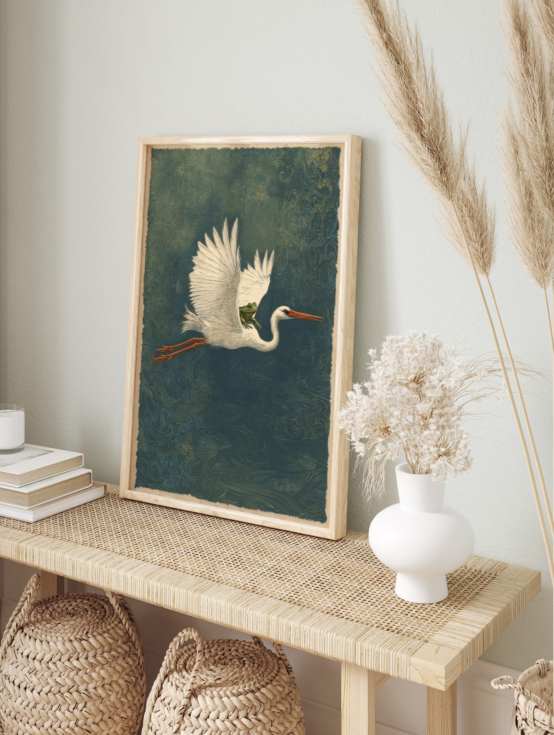Illustrative print of a white heron flying horizontally with a green frog on its back against, in an alternate framed mockup