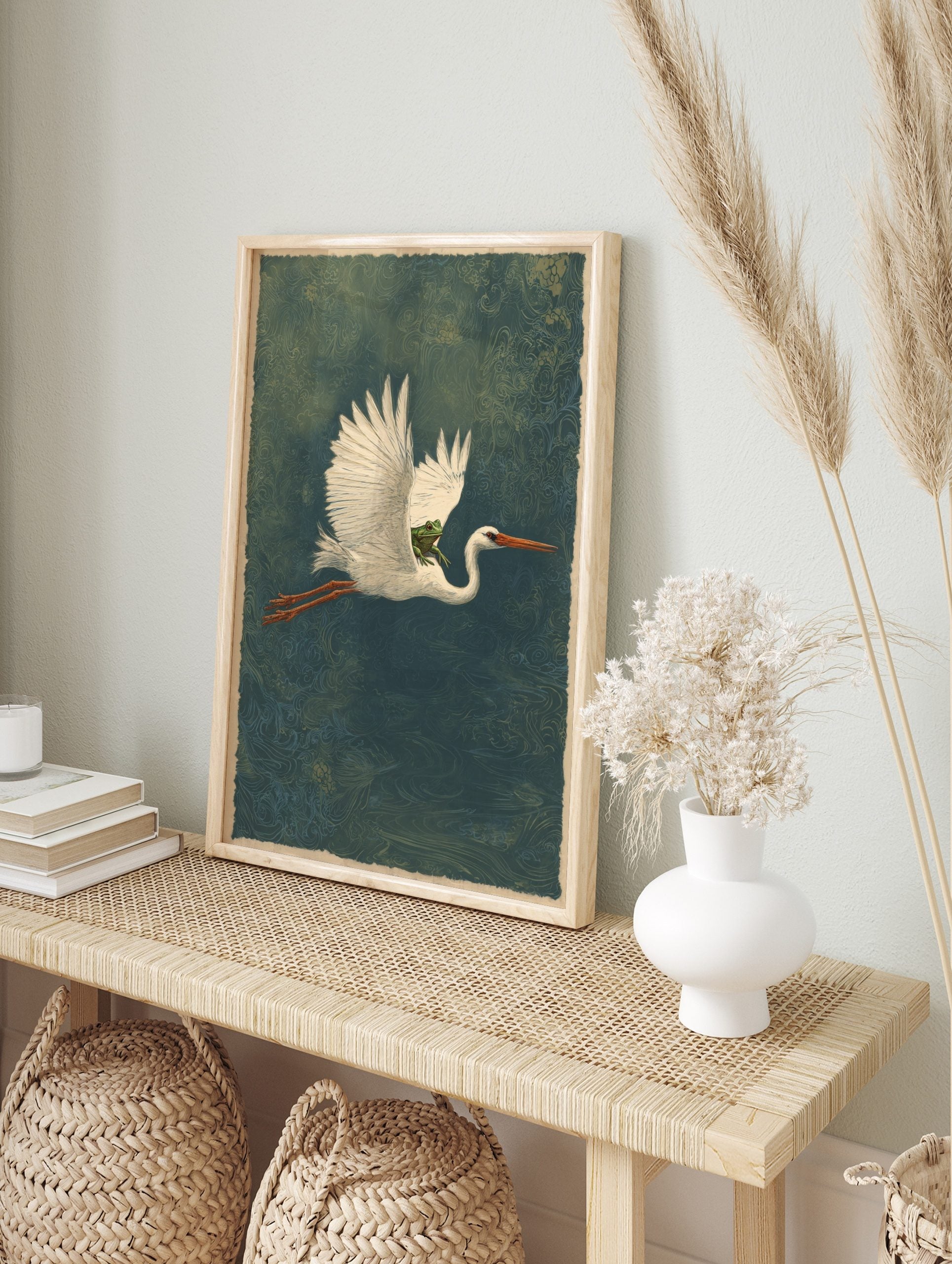 Illustrative white heron in flight carrying a green frog on its back, deep teal patterned, in an alternate framed mockup