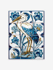 Illustrative white heron bird with blue feathers and golden legs, surrounded by blue flowers and reeds on ceramic tiles