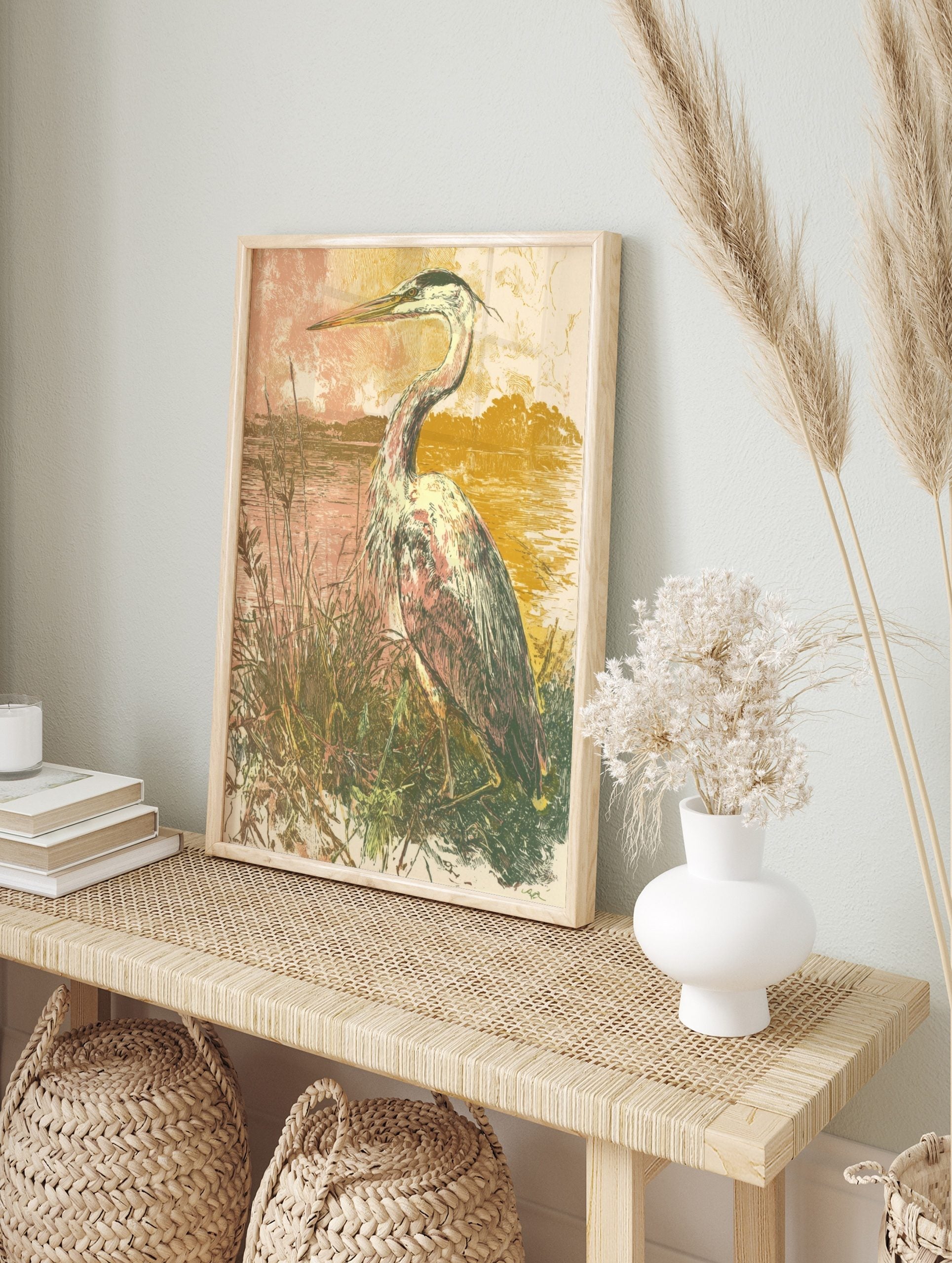 Illustrative art print of a heron bird standing in tall grasses by water, with a muted pink, in an alternate framed mockup