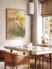 Illustrative art print of a heron bird standing in tall grasses by water, with a muted pink and, in a styled room mockup