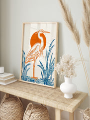 Illustrative heron bird print with orange outline, orange sun, and blue reeds on white, in an alternate framed mockup
