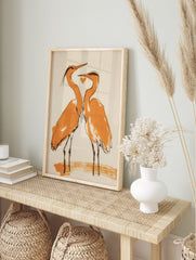 Minimalist illustration of two orange and black herons facing each other with a heart on a, in an alternate framed mockup