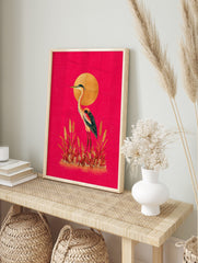 Illustrative heron or crane bird with golden sun and grasses on a hot pink background, in an alternate framed mockup
